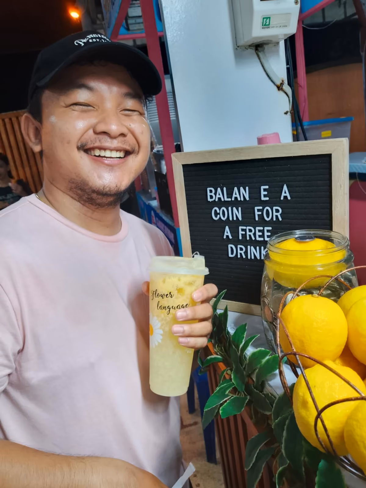A customer smiling and holding a Lemon Refresh drink beside the coin board at the stall
