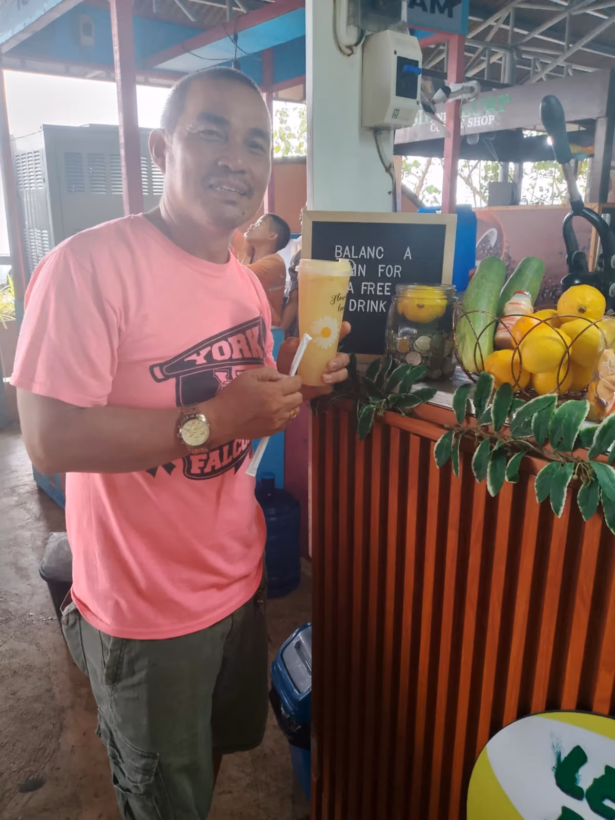 A customer holding a Lemon Refresh drink beside the coin board at the cart