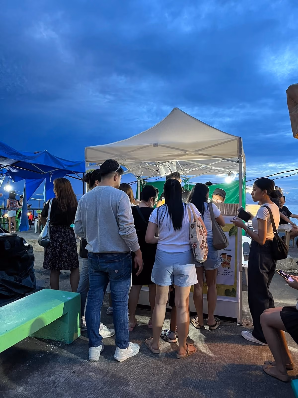 A queue of customers at the Lemon Refresh tent by the water at dusk
